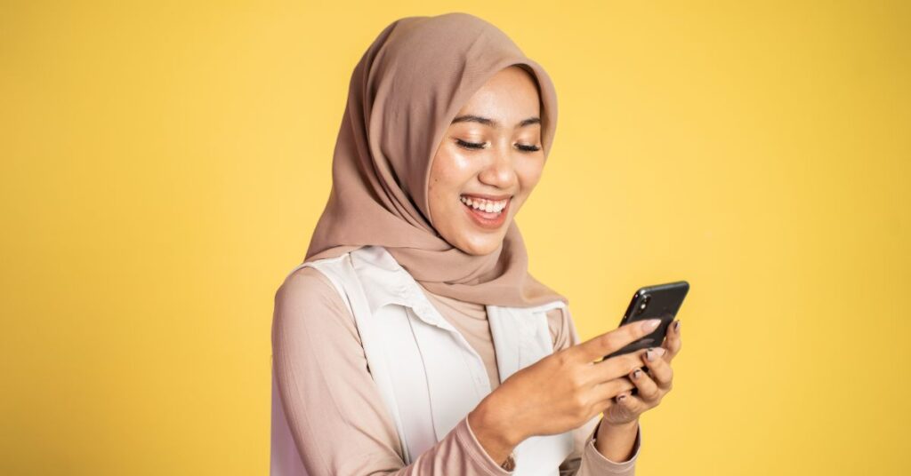 a Muslim girl using mobile in solid color background